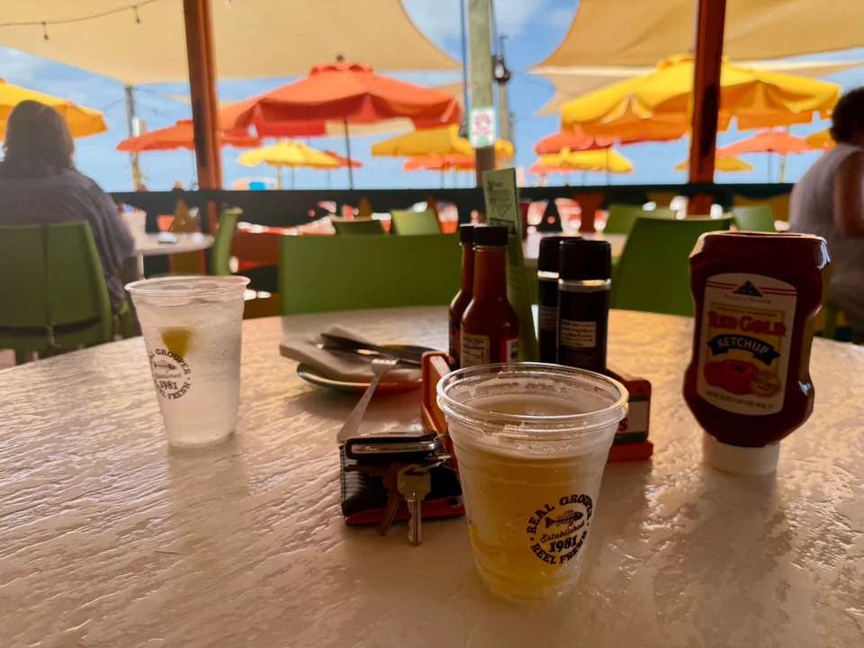 A table at Frenchy’s Rockaway Grill with branded cups, colorful umbrellas and a view toward the beach