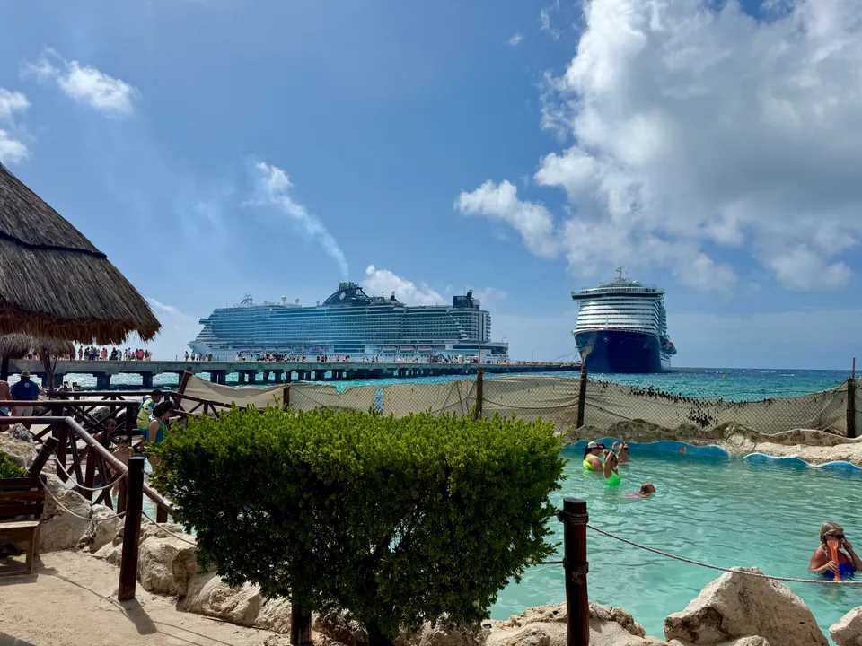 Pool and thatched-roof seating beside the Costa Maya waterfront, with ships beyond