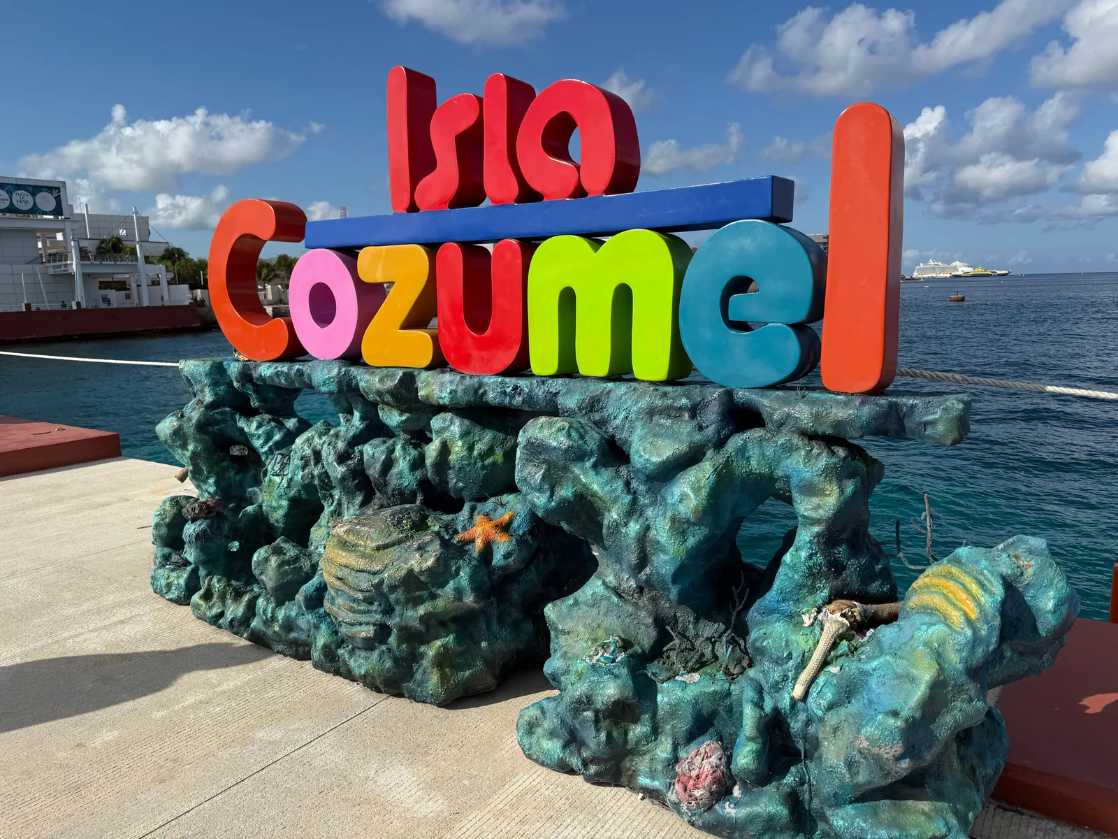 Colorful Isla Cozumel sign beside the sea and a docked cruise ship