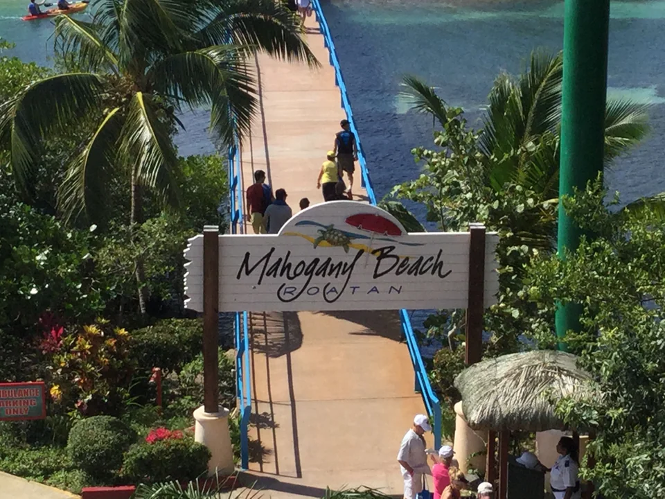 Mahogany Beach sign beside a blue-railed walkway and palm trees